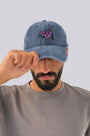 Man wearing a blue denim cap with a heart design on a plain background
