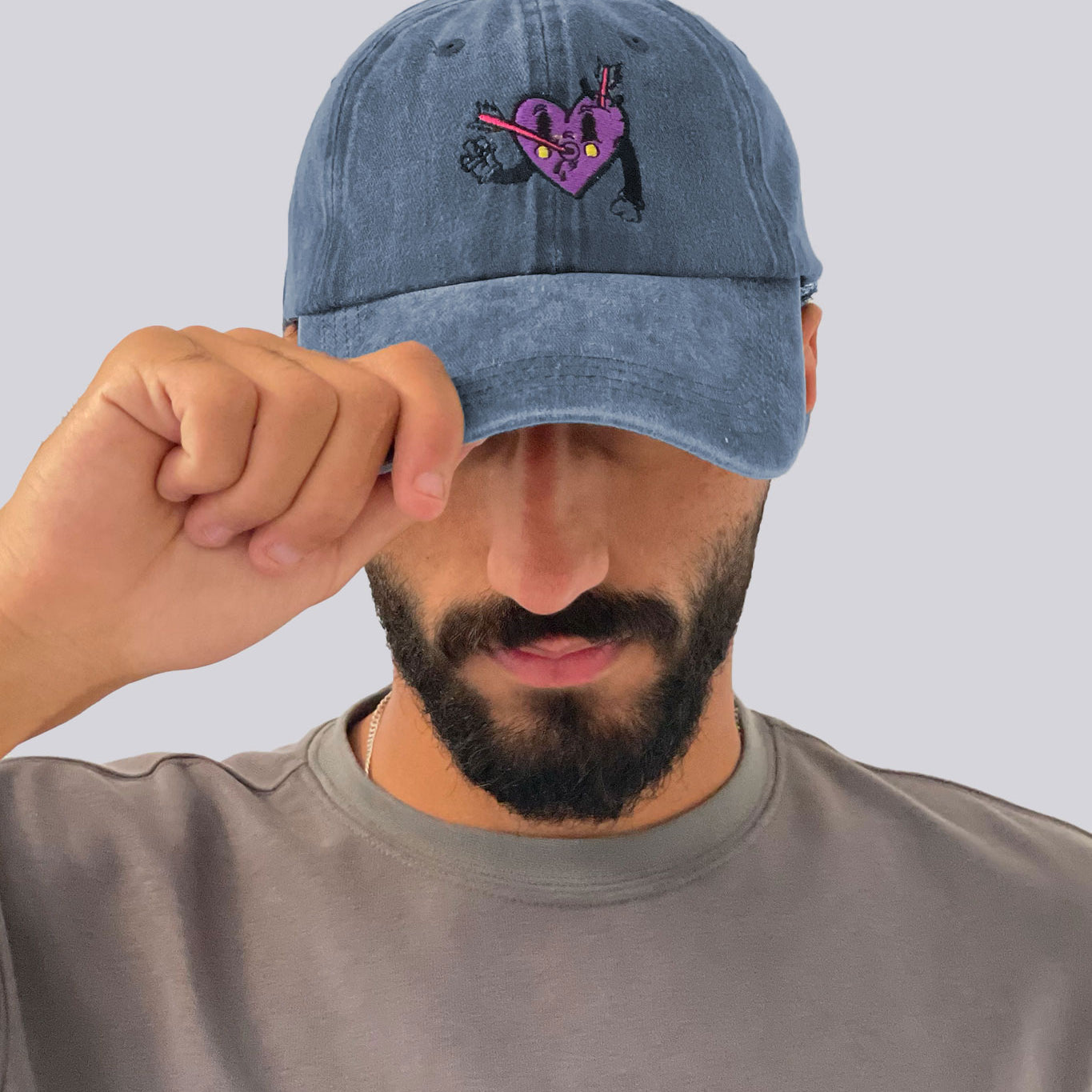 Man wearing a blue denim cap with a heart design on a plain background