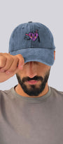 Man wearing a blue denim cap with a heart design on a plain background