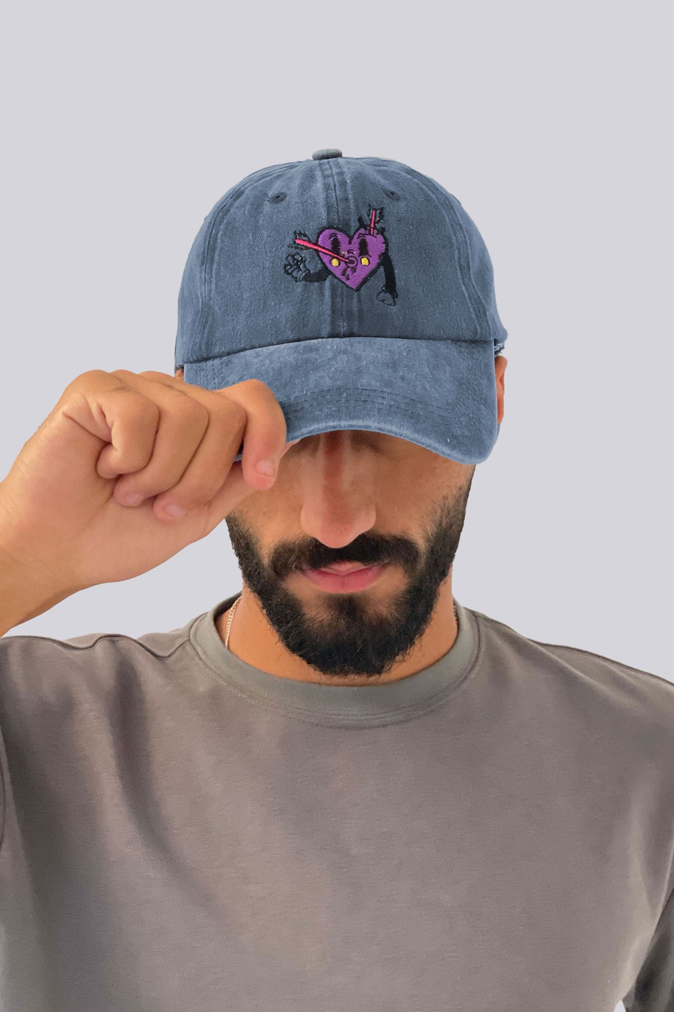 Man wearing a blue denim cap with a heart design on a plain background